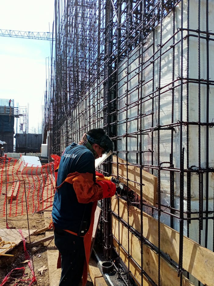 A construction worker welds metal frameworks at a busy building site, showcasing industrial safety.