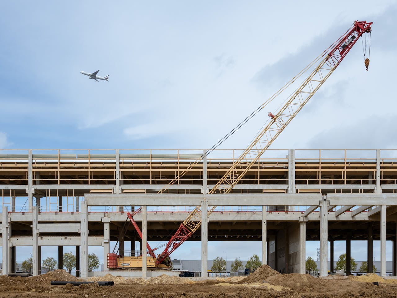 A large crane at a construction site with a plane flying overhead, set against a clear sky.