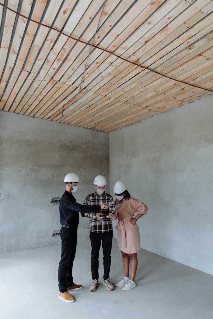 Engineers wearing hard hats review building plans in an unfinished room, discussing construction strategy.